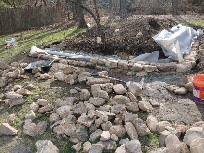 Stone drainage installation taking shape beside a wooded property